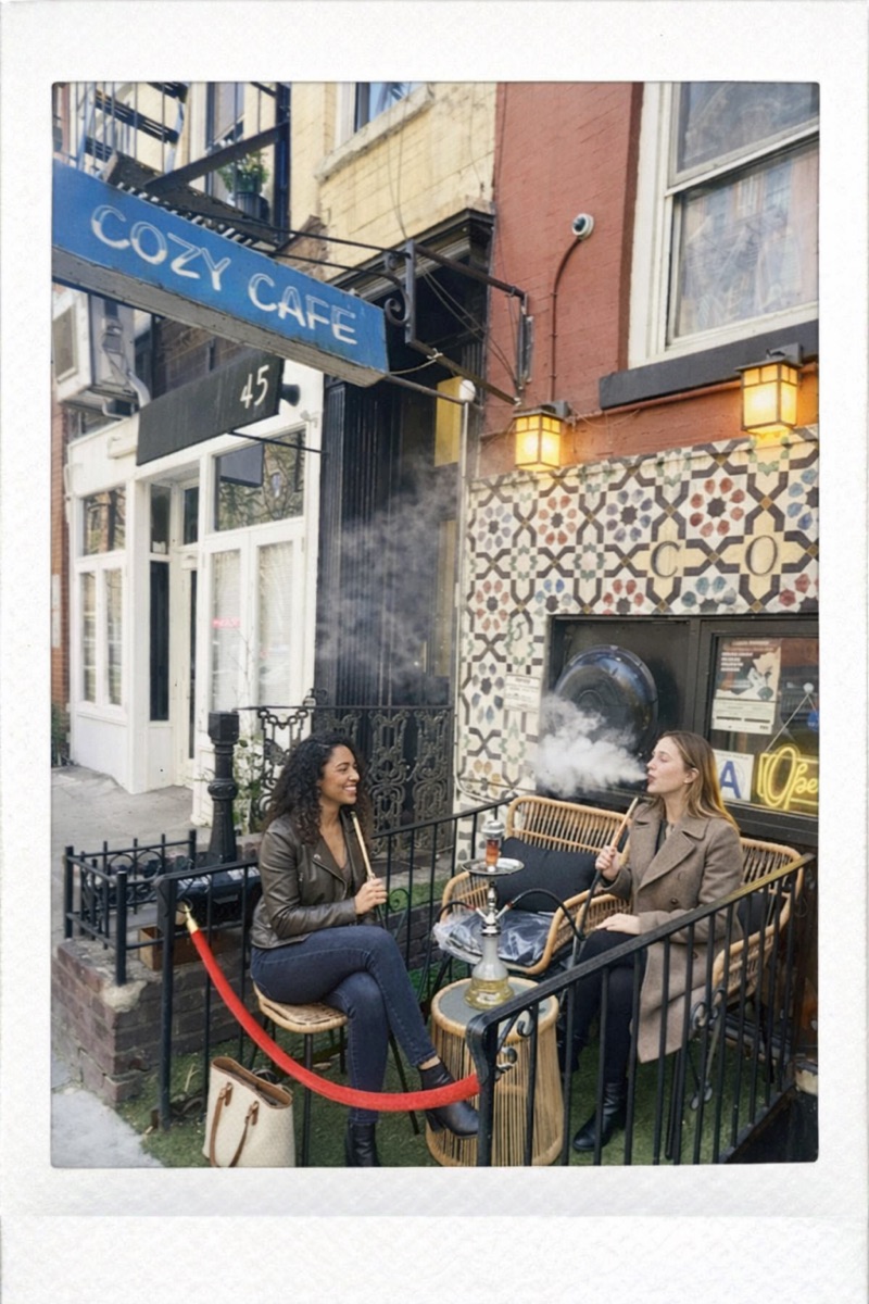 Cozy Cafe NYC exterior — mosaic tile wall, blue sign, patio seating